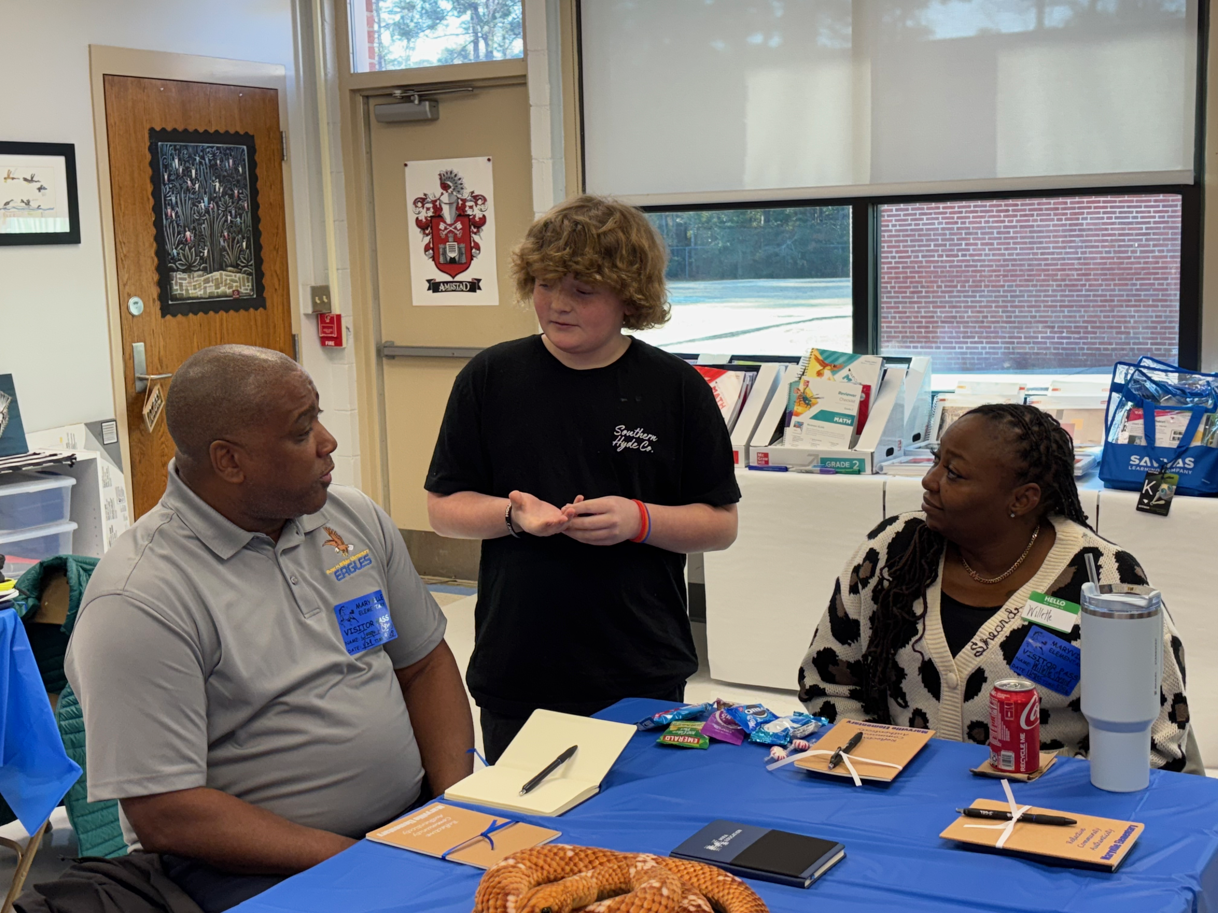 Two seated adults talk to a student about collective leadership in practice at his school.